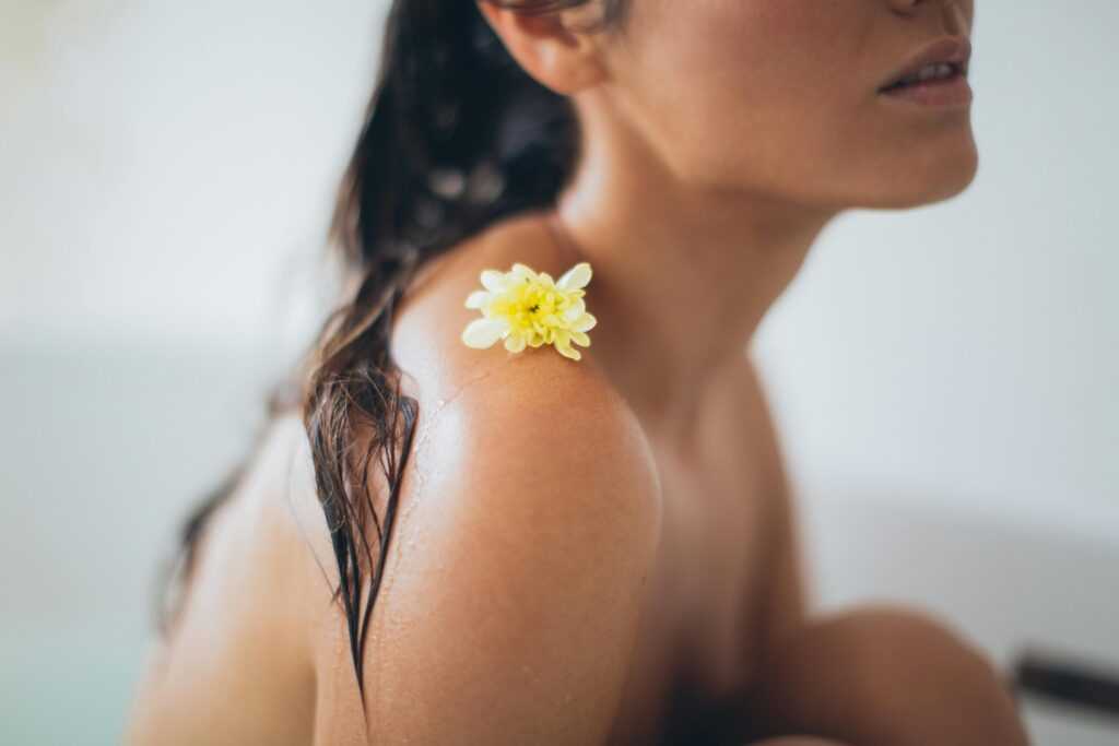 Close-up of a woman relaxing in a bath with a yellow flower on her shoulder.